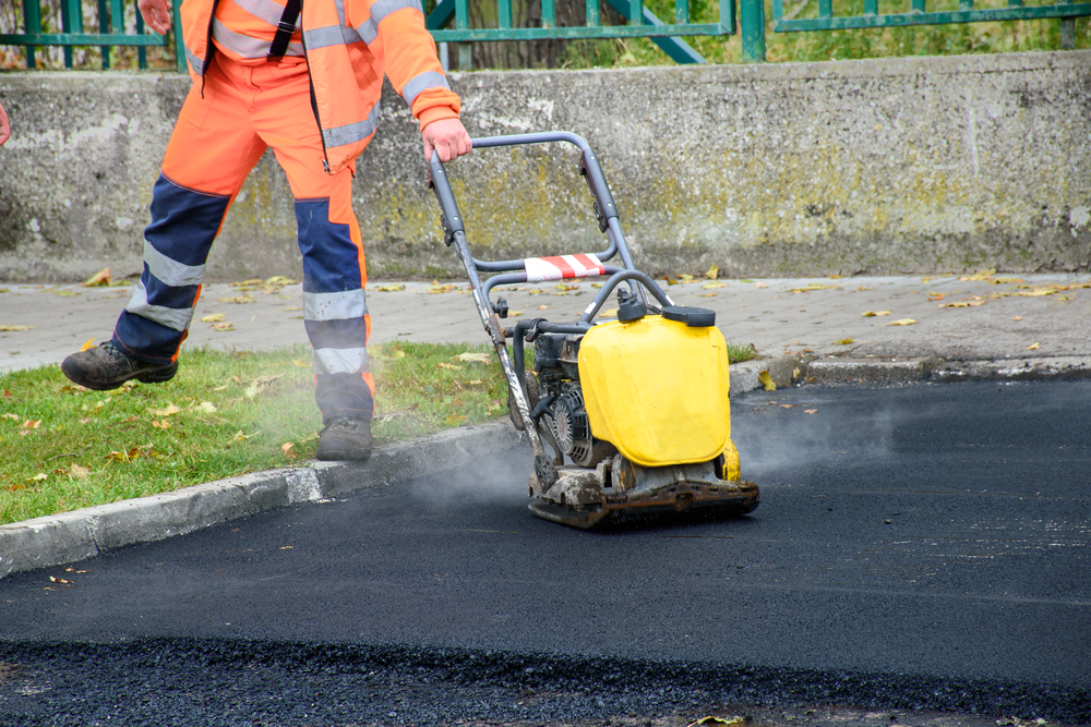 Paving,worker,uses,vibratory,plate,compactor,to,compact,new,asphalt